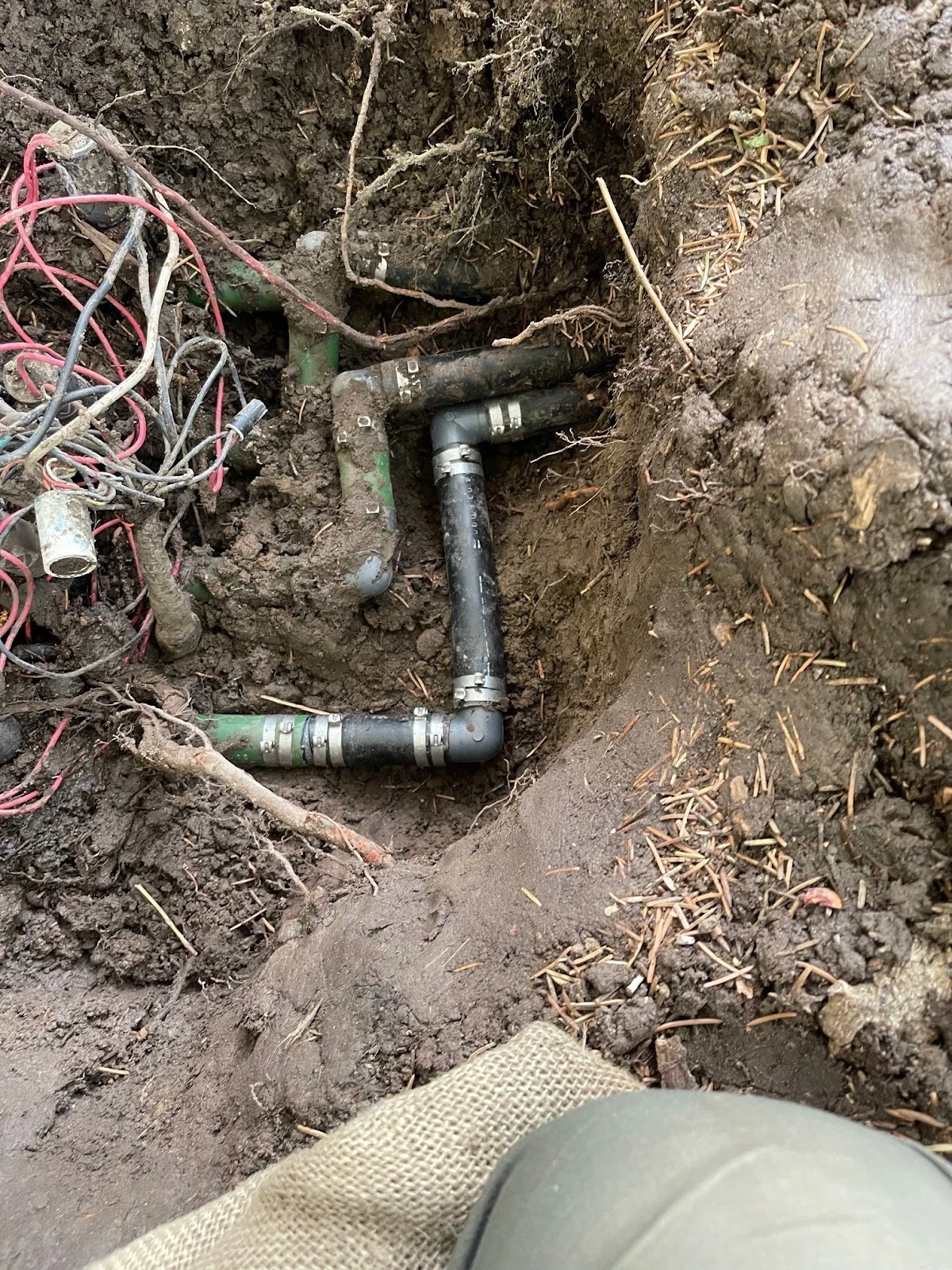 Exposed irrigation pipe and fittings in a repair trench, from Outdoor Legacy’s owner-uploaded photos